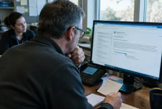 Employee carefully verifies a suspicious email in an understated IT support room.